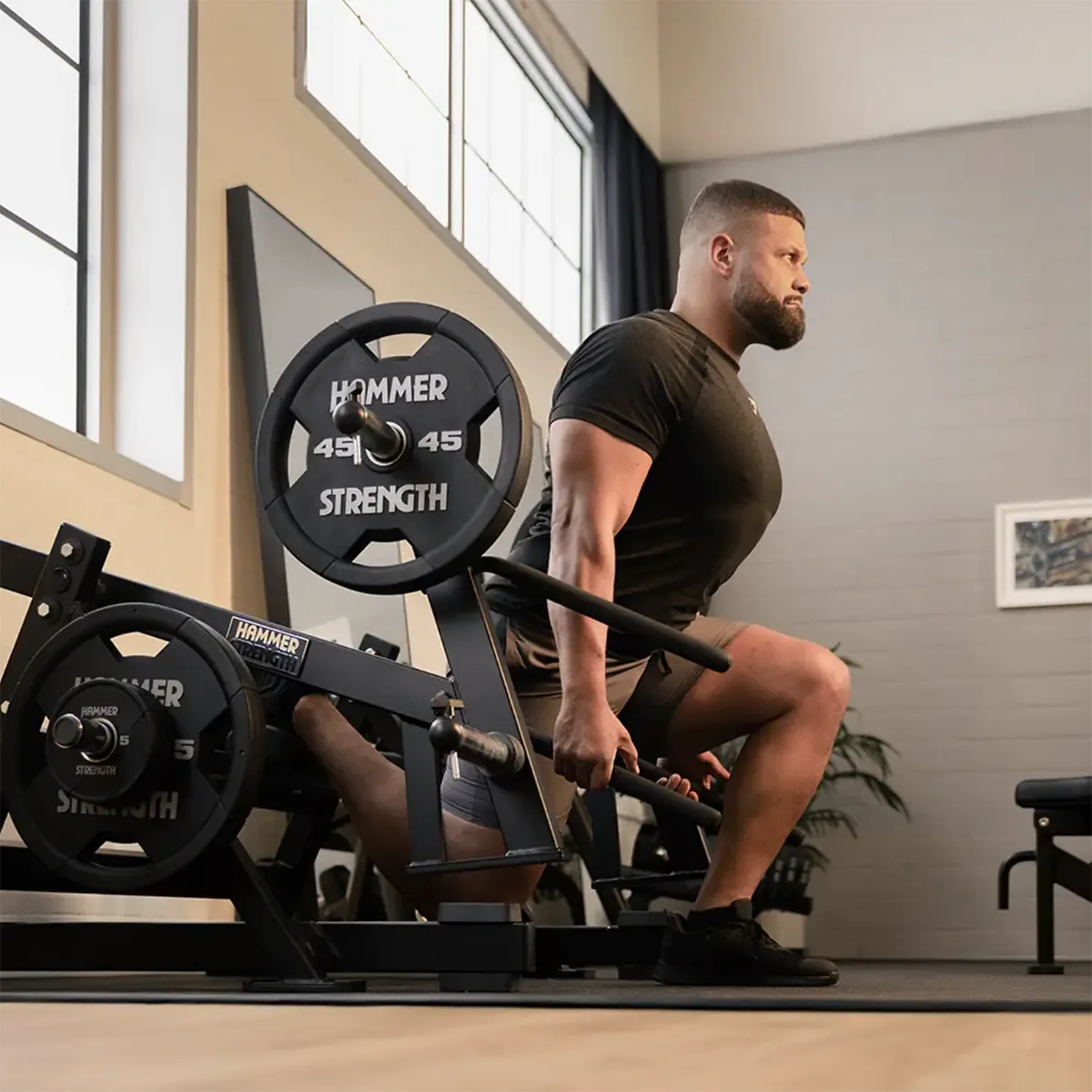 Plate-loaded lower body machine with angled handles and single-leg squat pad