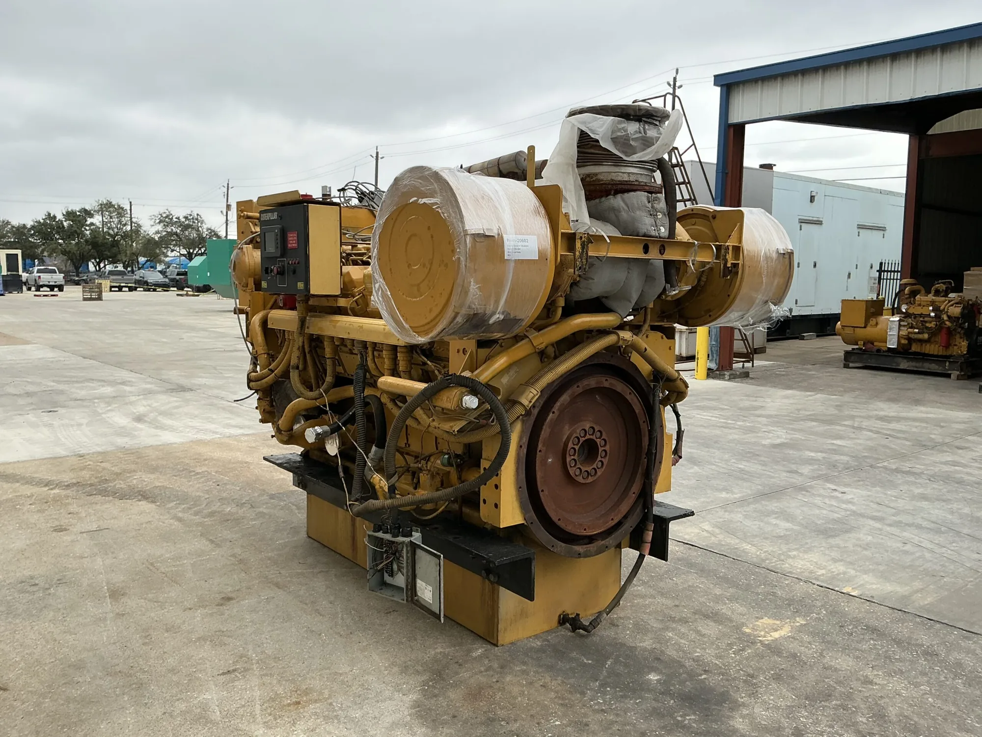 Yellow industrial generator with black control panel and red emergency stop, mounted on a yellow frame with a wrapped cylindrical drum