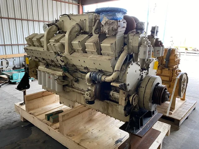 Industrial diesel engine on a wooden pallet, beige with multiple hoses and a prominent exhaust manifold